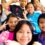 A young woman stands with a group of children as they smile and pose for a photo.