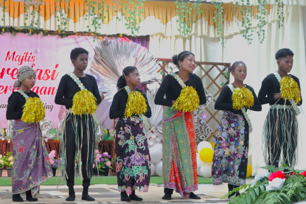 A group of six Orang Asli Bateq children dressed in traditional attire perform a cultural dance on stage.