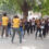 A group of young girls participates in an outdoor self-defense training session led by two instructors in yellow shirts.